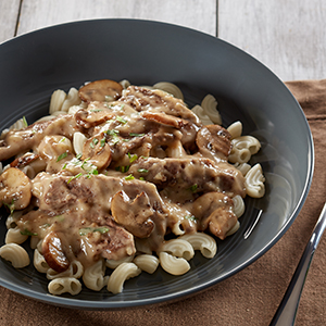 A black bowl on a brown placemat holds a serving of Gluten Free Beef Stroganoff