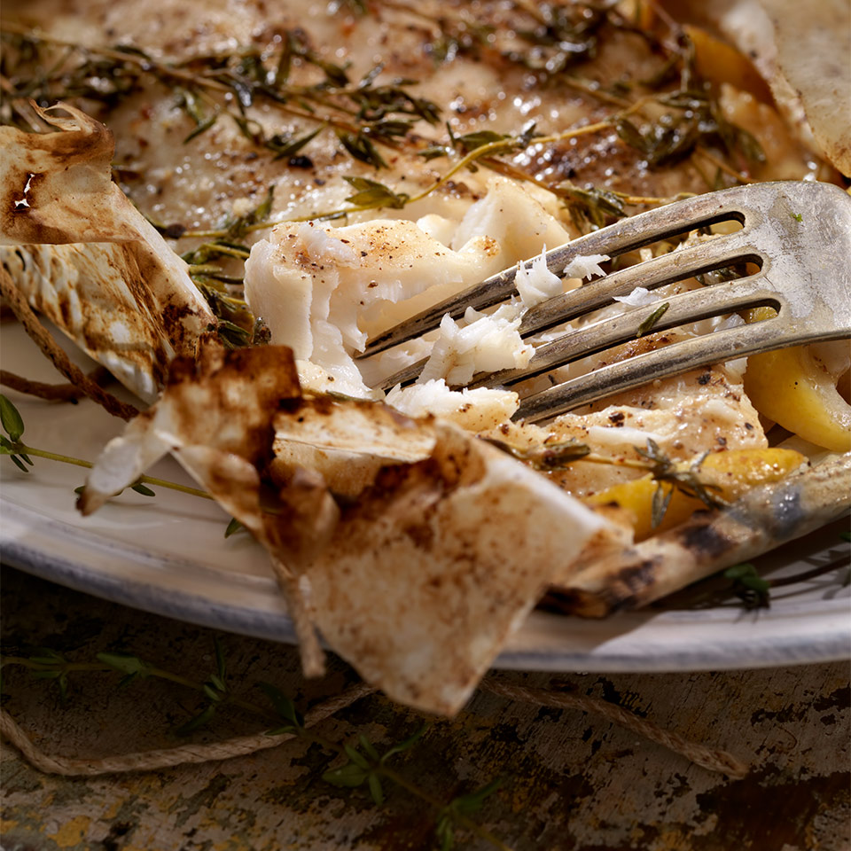A closeup of a fork making its way through a flaky dish of Cod en Papillote.