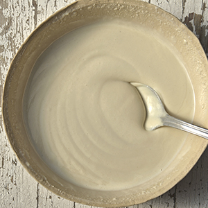 A closeup of a tan bowl on a rustic wooden table holding Organic Tahini