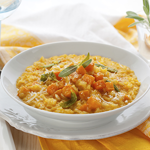 A white ceramic bowl placed on a white plate, with the bowl holding Spiced Quinoa Pumpkin Risotto.