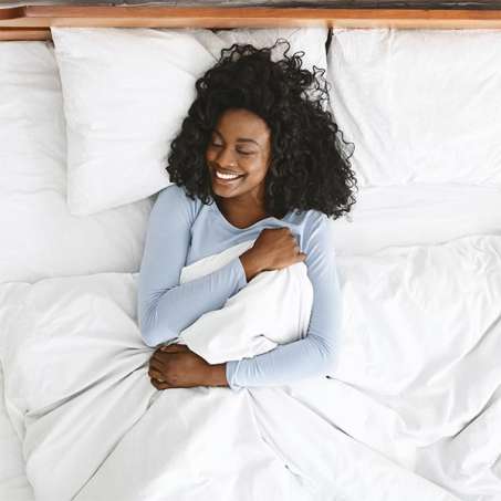 dark skinned, female presenting person smiling lying in bed