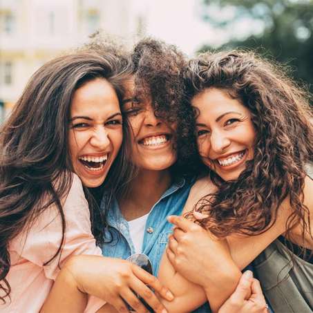 three multiracial female presenting people embracing and smiling 