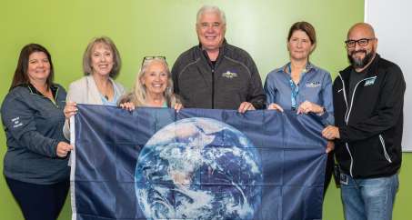 Jim Emmy, CEO of NOW along with NOW employees holding an blue flag with an image of the earth