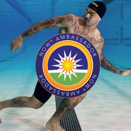 Bruno walking underwater in a black swim cap and black shorts with the NOW Ambassador logo overlayed