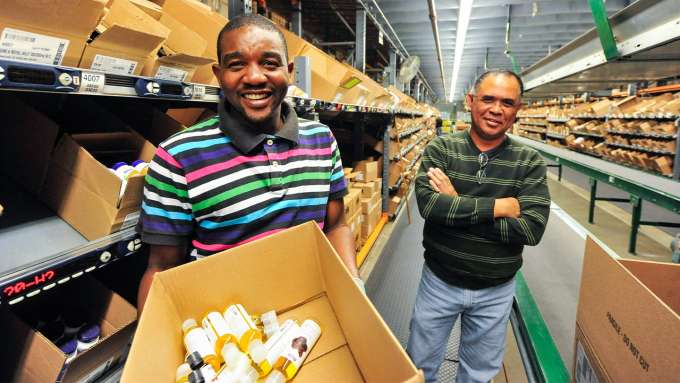 two factory worker men of different races smiling and holding a box o NOW products