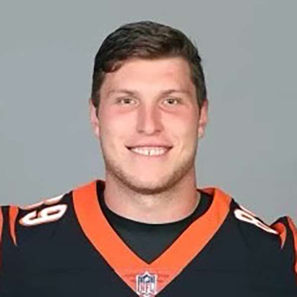 Drew Sample is smiling in this headshot photo. He has light skin and an oval shaped face with a prominent square jaw and has brown eyes and short straight dark brown hair parted to the right. He is wearing a dark brown Bengals jersey with orange trim at the v neck and the number sixty nine in white on each shoulder.