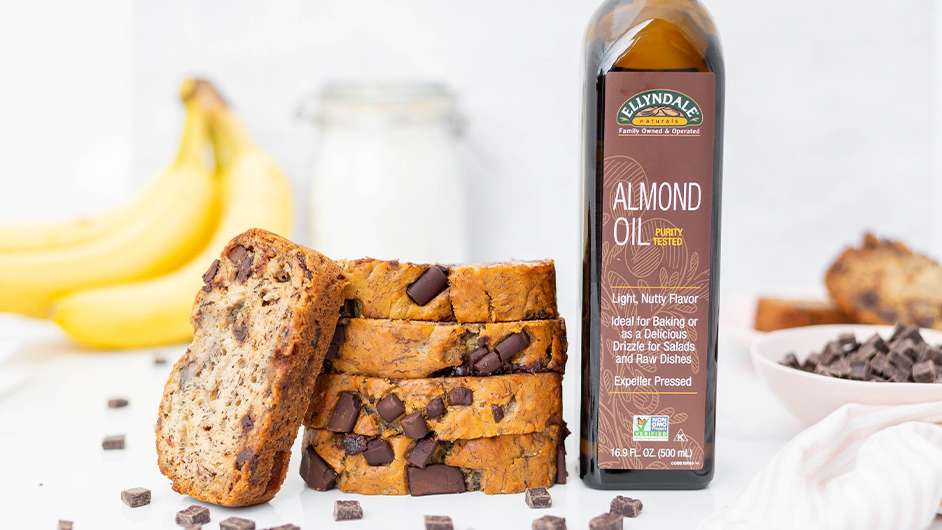 chocolate chunk banana bread slices stacked next to a bottle almond oil