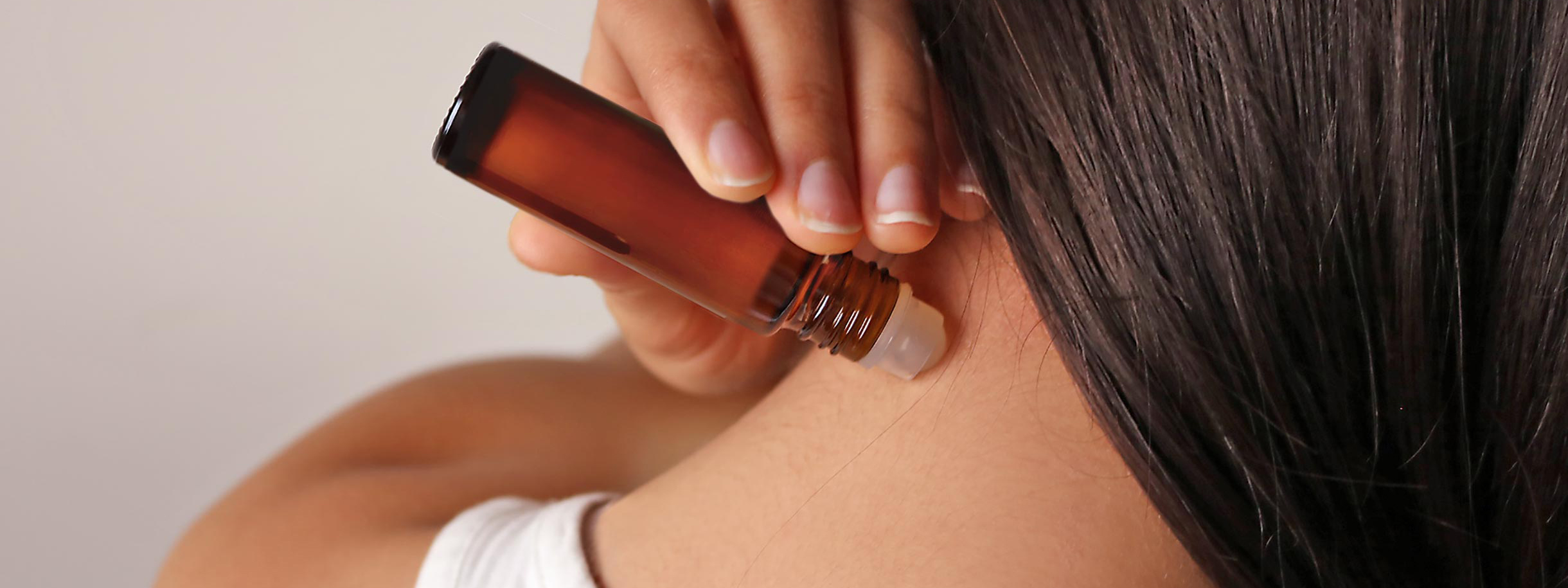 light skinned, female presenting person applying roll on essential oils to neck