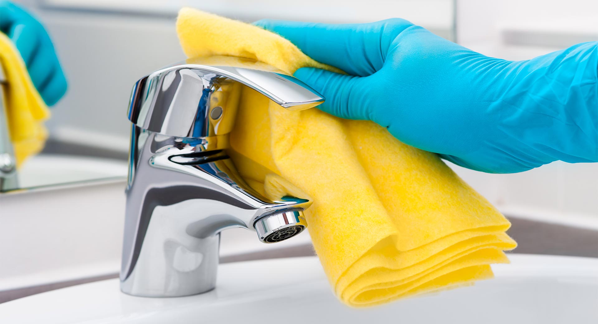 yellow towel cleaning a bathroom faucet wearing blue rubber gloves. 