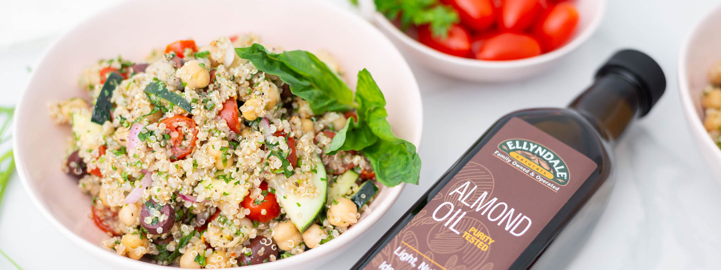 a white bowl with Greek quinoa salad, various colors and a bottle of NOW almond oil laying next to it