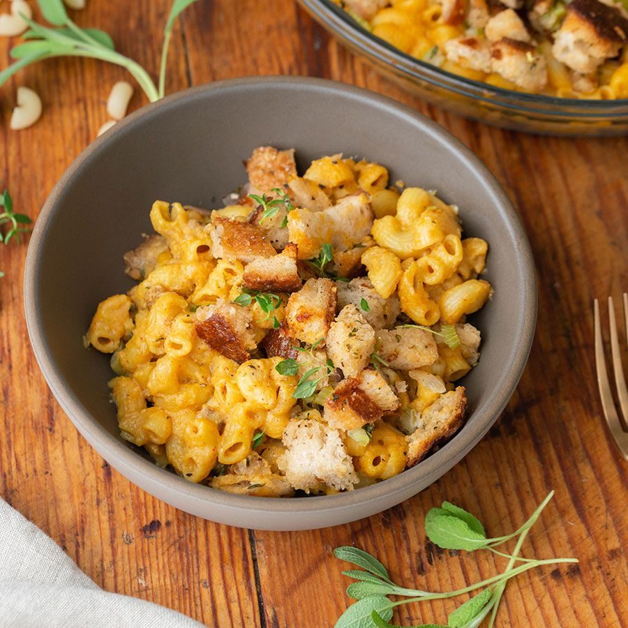 brown bowl with stuffing-topped macaroni and cheese with a fork on the right side all on a wooden table