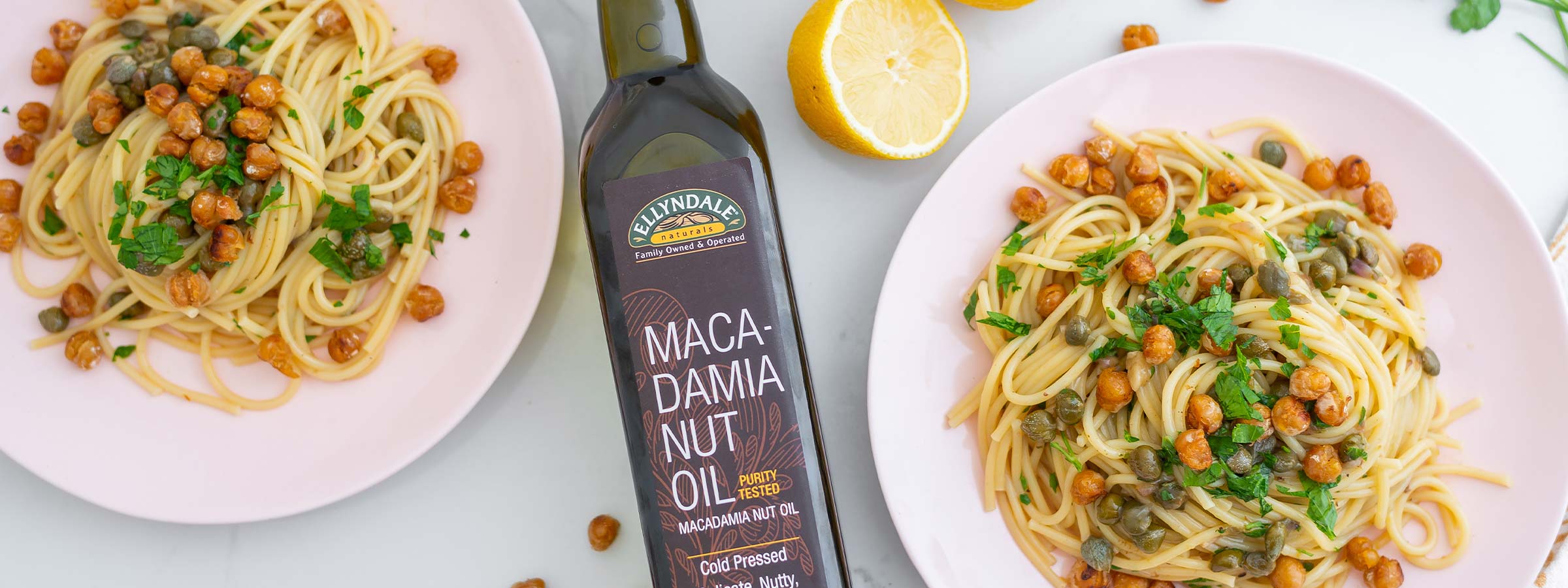 two bowls of lemon caper pasta with crispy chickpeas on top with a bottle of ellyndale macadamia nut oil inbetween 