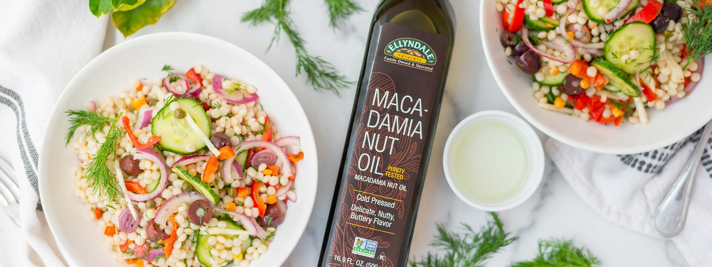 two bowls of mediterranean salads with a bottle of ellyndale macadamia nut oil in between 