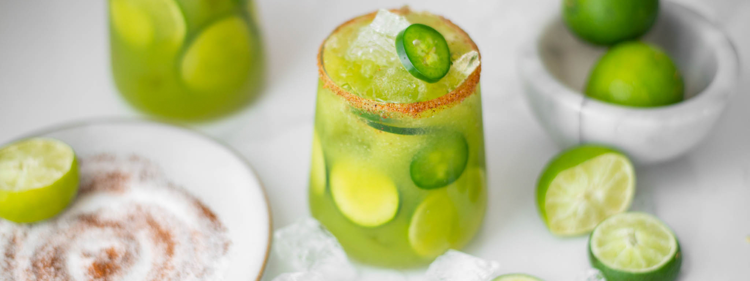 glass filled with a cucumber, jalapeno mocktail surrounded by limes