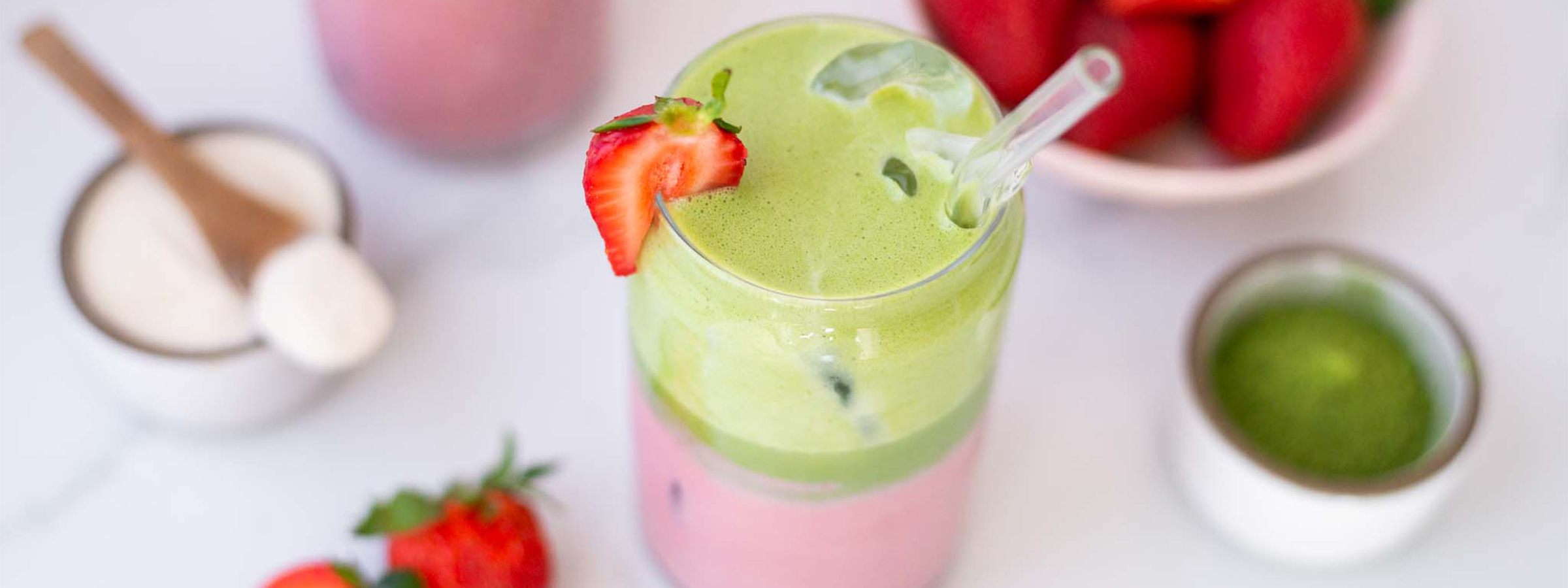 glass of strawberry matcha with strawberries, matcha, and oat milk powder around it