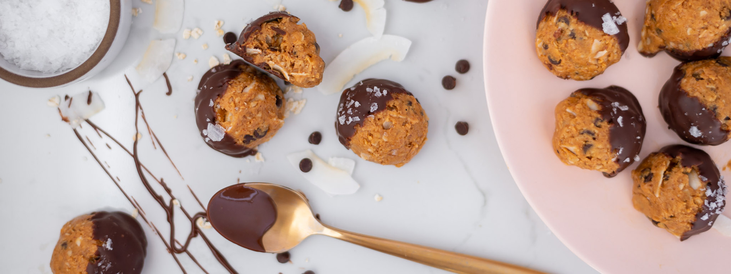 top view of Chocolate-Dipped Caramel Peanut Butter Oat Bites with spoon of chocolate and coconut oil