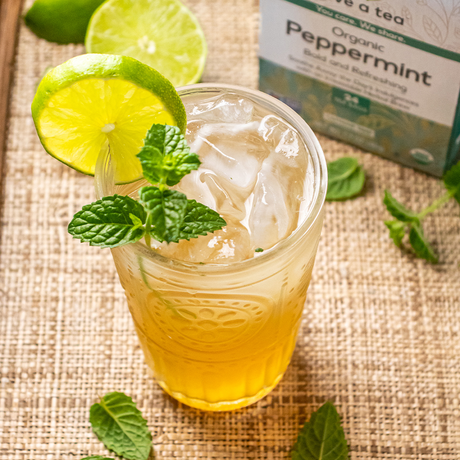 slight top view of a minty tea mocktail with a lime wedge and sprig of mint in a glass next to NOW peppermint tea