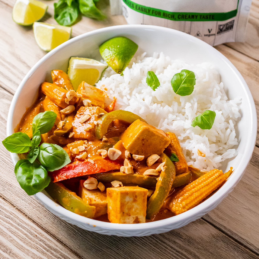 top view of oat milk powder next to a bowl of thai peanut curry with tofu and rice