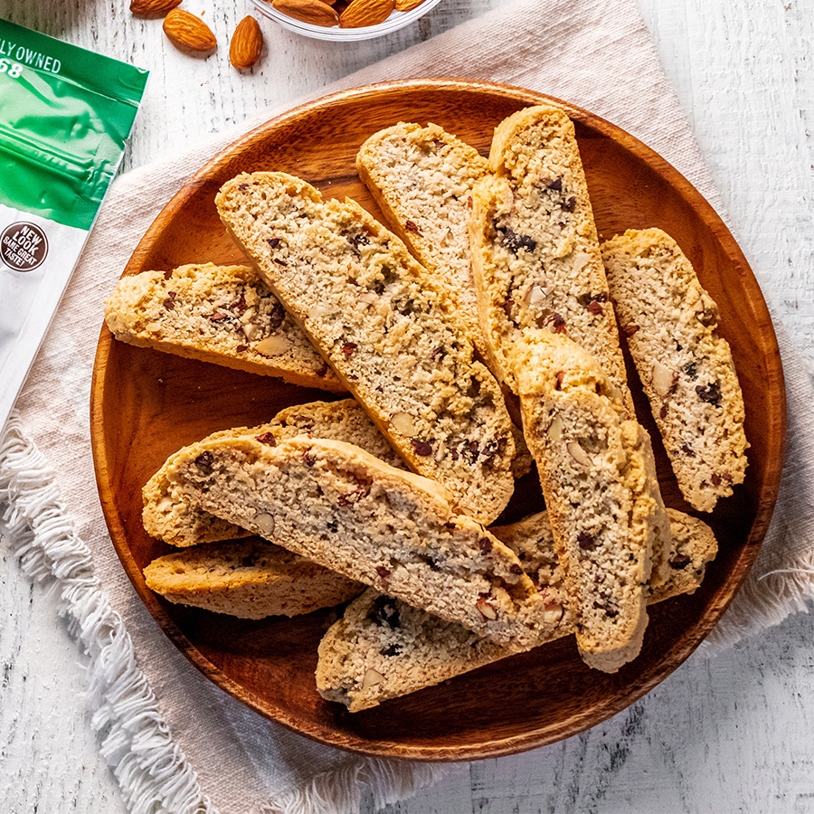 top view of Almond and Cacao Nib Biscotti on brown plate next to bag of NOW Raw Cacao Nibs