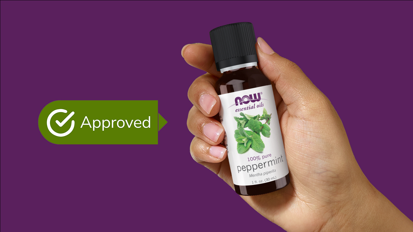 A hand holds a bottle of NOW Foods Peppermint Essential Oil, which is has a checkmark and the word Approved beside it.