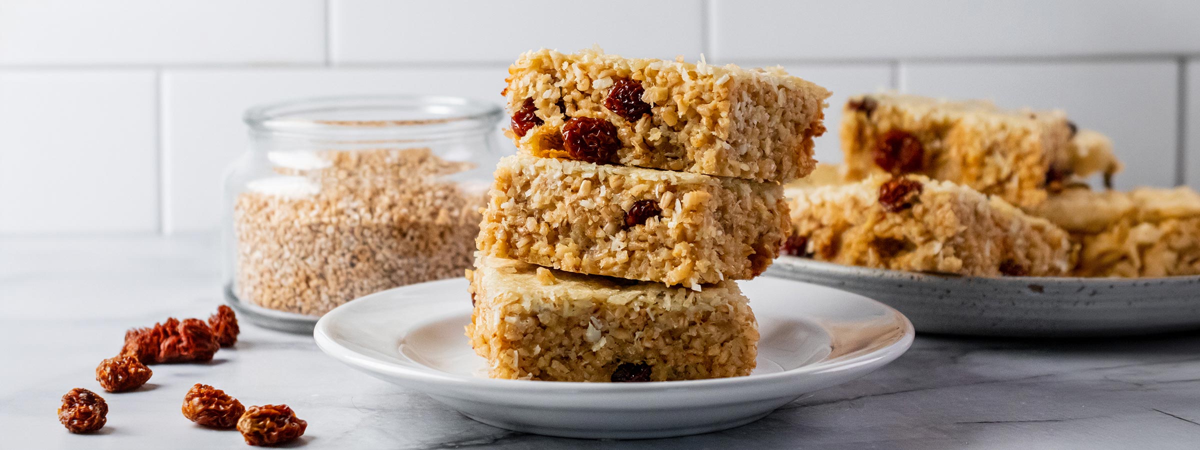 3 steel cut oat golden and coconut bar square stacked on white plate