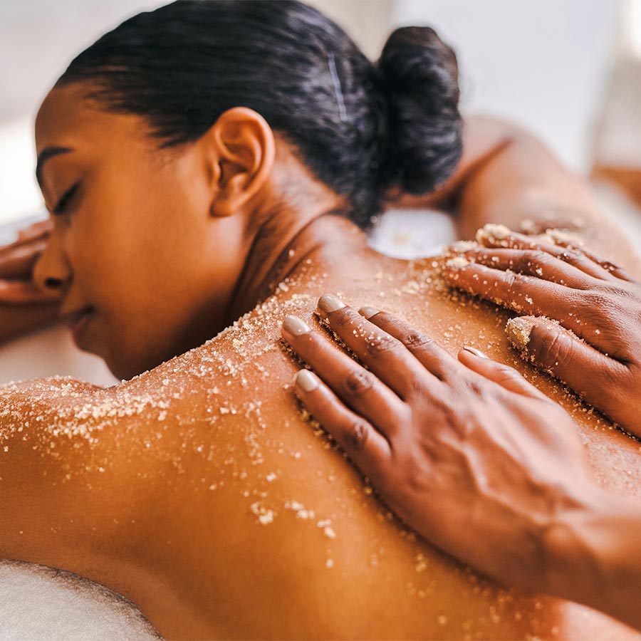 Dark skinned female presenting person getting an exfoliating with sugar scrub