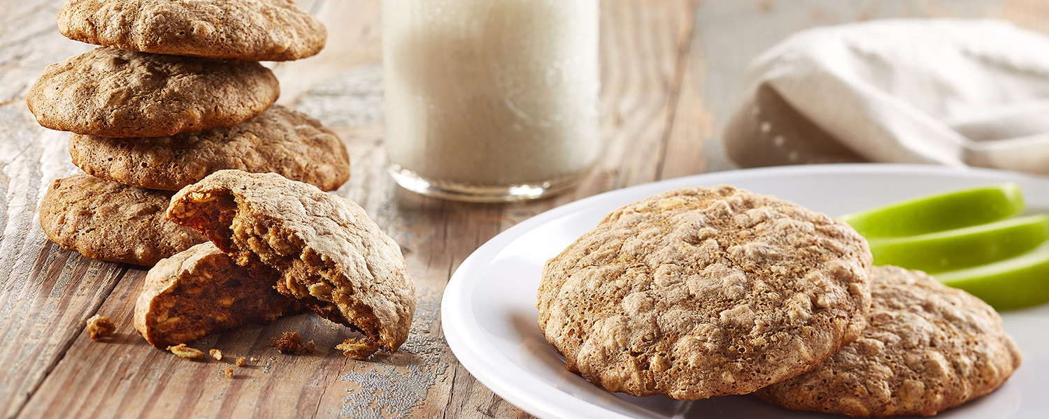 A rustic wooden table with flaky, light-brown Apple Oatmeal Breakfast Cookies on a white plate.