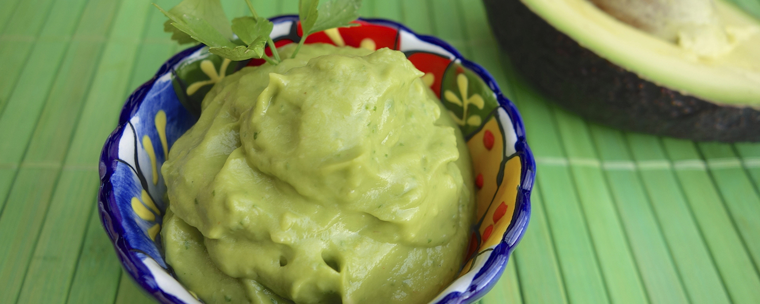 A colorful ceramic bowl placed on a green wooden table is filled with Avocado Sauce