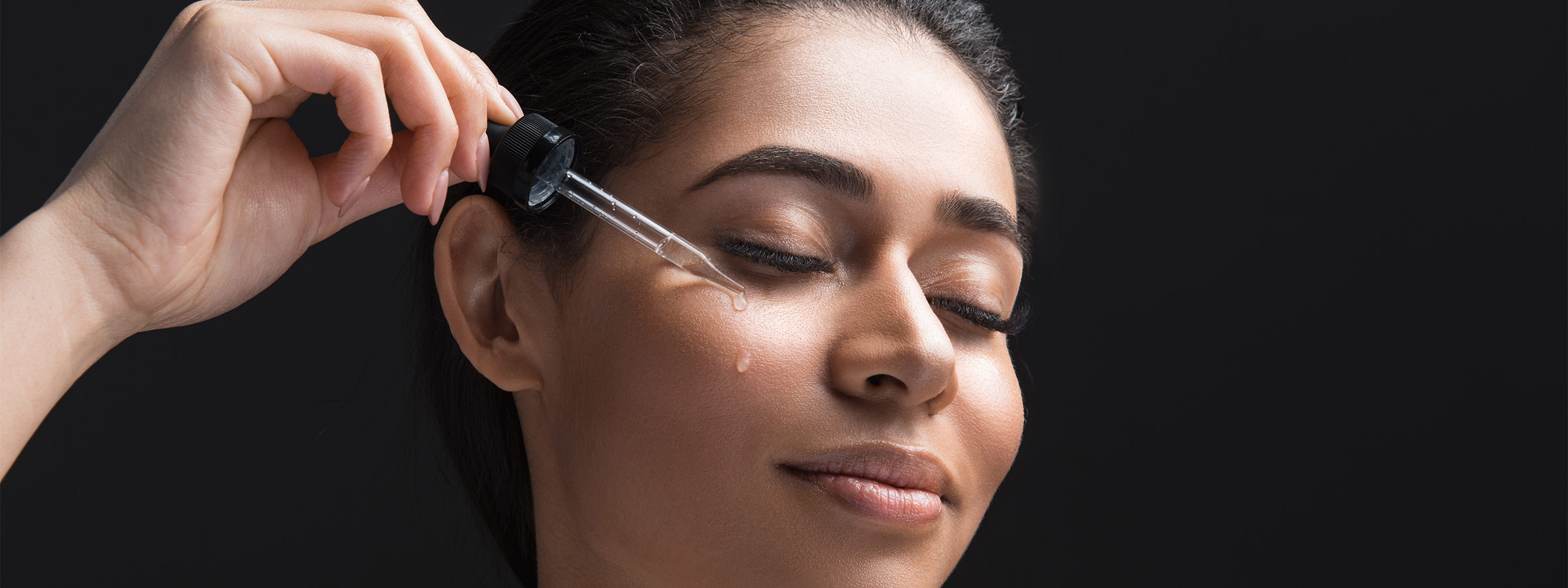 light-skinned, female-presenting person applying drops of skin serum to her face