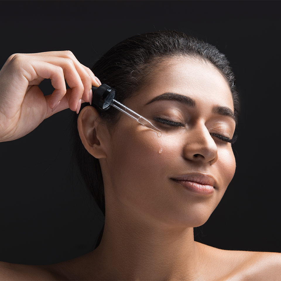 light-skinned, female-presenting person applying drops of skin serum to her face