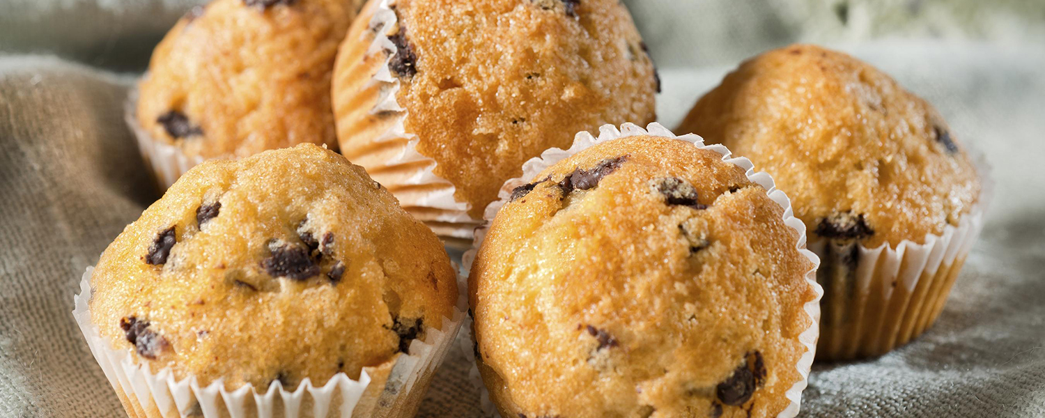 Several fluffy Blueberry Flax Muffins are placed on a table in their wrappers.