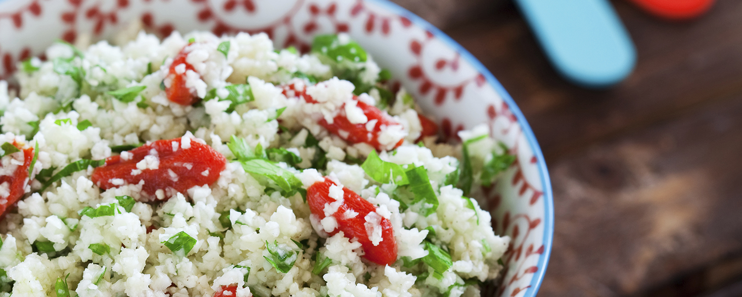 A white ceramic bowl with red and blue floral decorations is filled with Cauliflower Couscous