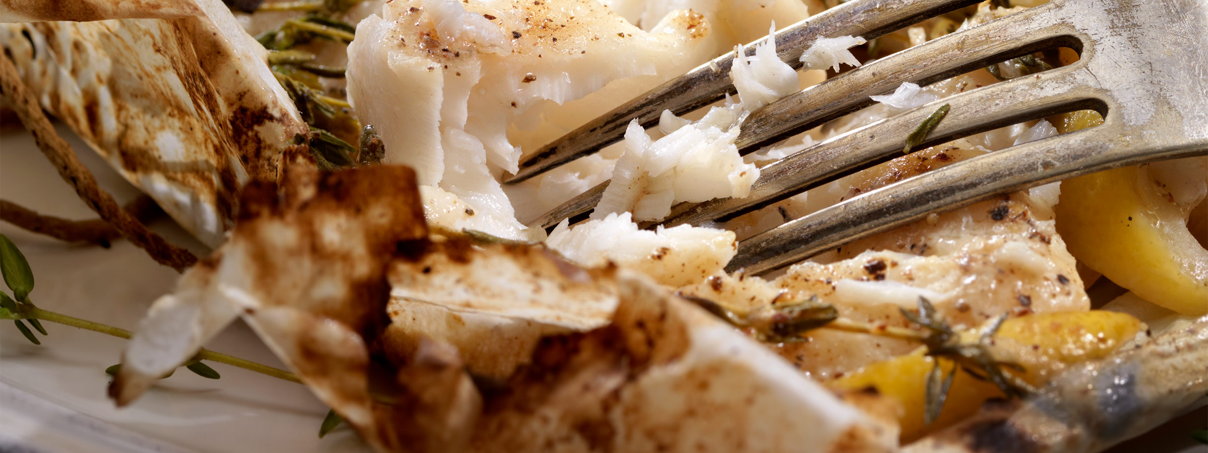A closeup of a fork making its way through a flaky dish of Cod en Papillote.