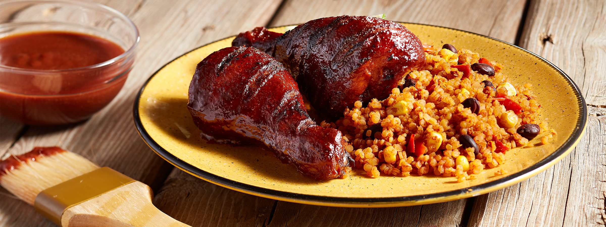 A yellow plate on a wooden table holds servings of Grilled BBQ Chicken with Quinoa.