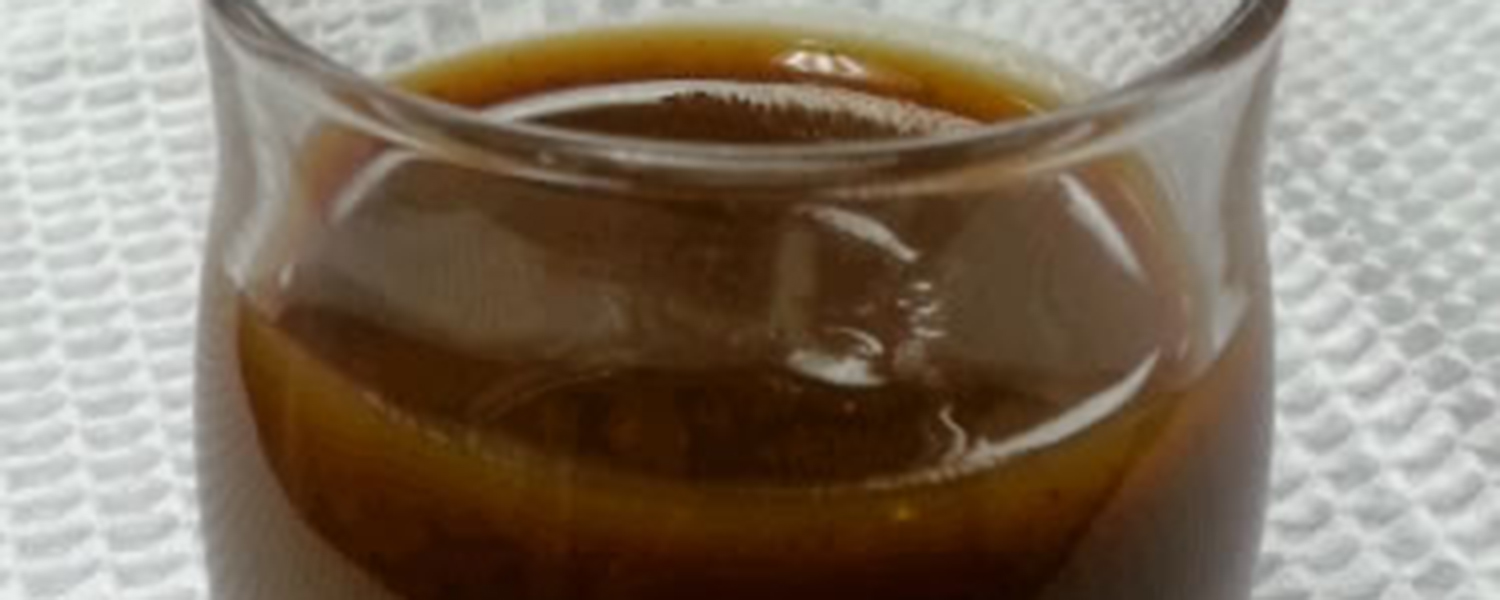 A closeup of a drinking glass filled with a serving of dark brown Spiced Pumpkin Syrup