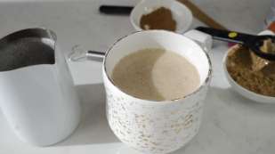 white coffee cup with tan colored liquid inside, small white cream pitcher to the left all on a white counter top