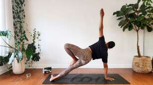 medium skin toned female presenting person doing a yoga pose on a black yoga mat 