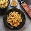 top view image of nutty peanut noodles in black bowl next to bottle of rice bran oil