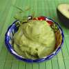 A colorful ceramic bowl placed on a green wooden table is filled with Avocado Sauce