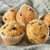 Several fluffy Blueberry Flax Muffins are placed on a table in their wrappers.