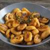 A grey dinner bowl on a wooden table is filled with golden-brown Butternut Squash Dumplings.