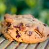 A Chocolate Cherry Blondie Cookie sits on a wooden table outdoors.