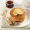 A stack of Going Bananas Pancakes on a white ceramic plate. Slices of banana top the pancakes.