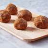 A wooden platter on a marble countertop holding several Pom-Berry Nut Energy Bites.