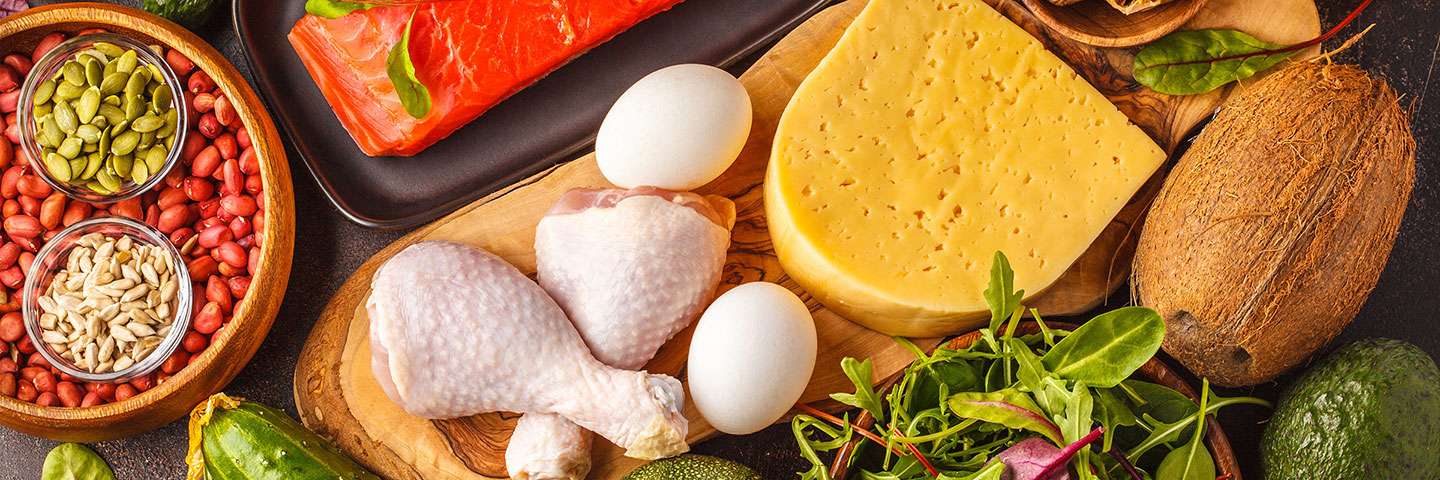 several food products layed out on a table photographed from a top view - raw chicken legs, eggs, bowl of grain, green veggies