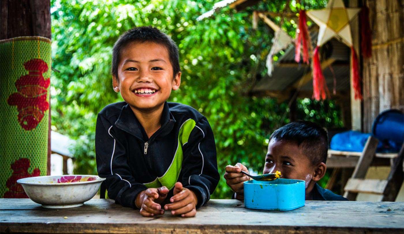 A medium-skinned, male-presenting child smiles wide and leans against a counter.