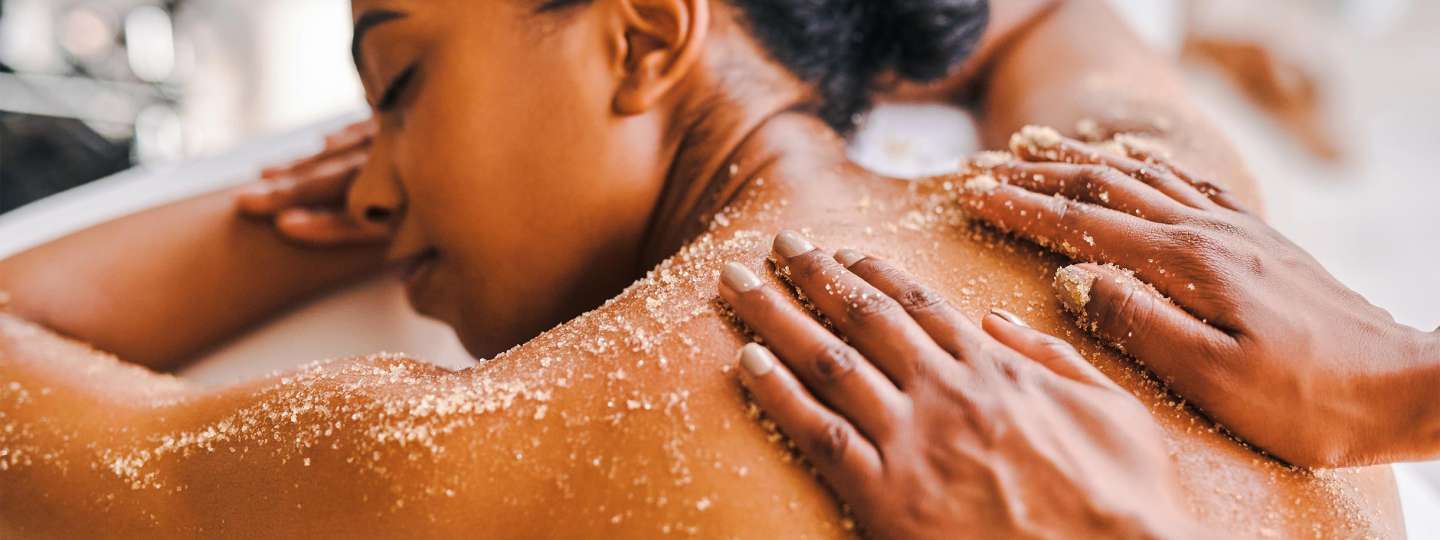 Dark skinned female presenting person getting an exfoliating with sugar scrub