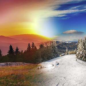 sun coming up over a snowy scene with mountains in the background and pine trees framing a snow covered field