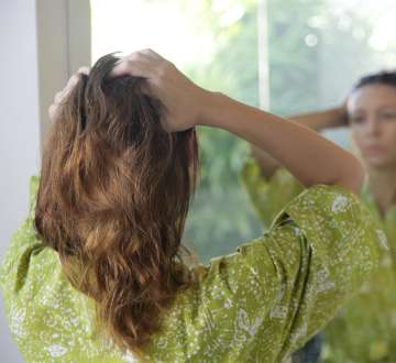 light skinned female presenting person looking in a mirror adding Argan Oil to her hair