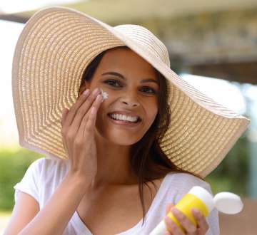 light skinned female presenting person in large brimmed hat applying sunblock 